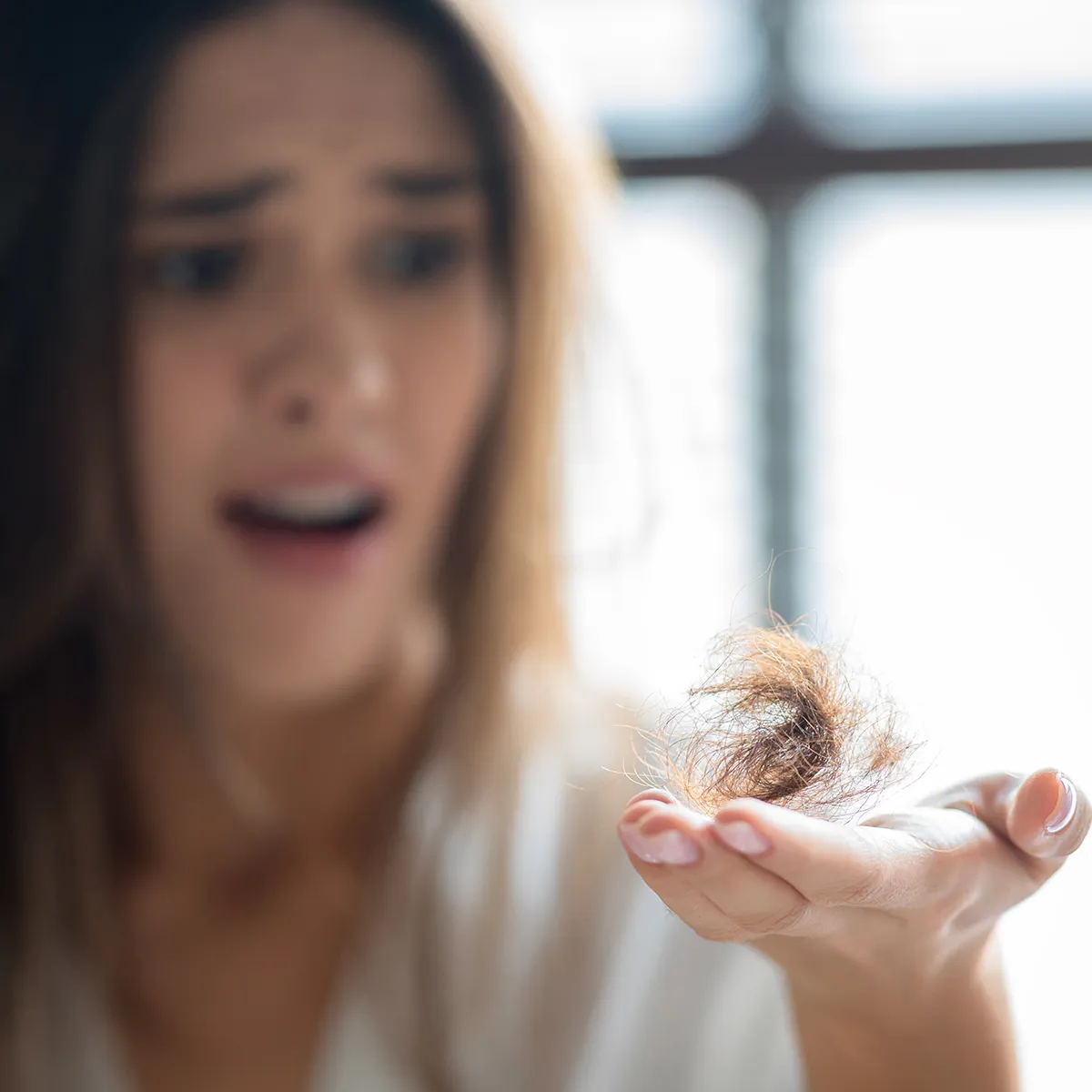 Woman looking at a clump of shed hair in her open palm with a distressed expression
